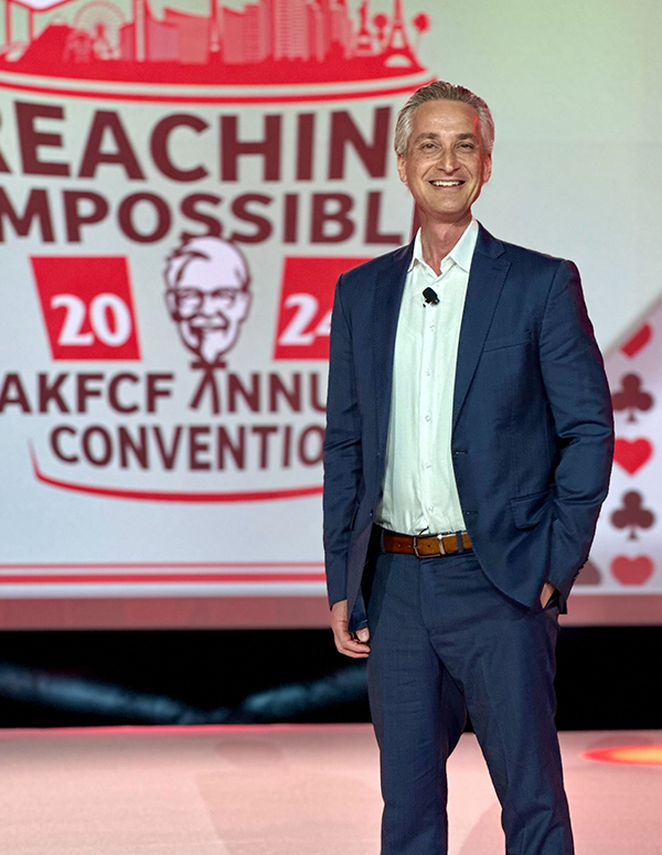 scott greenberg standing on stage in a blue suit in front of KFC logo
