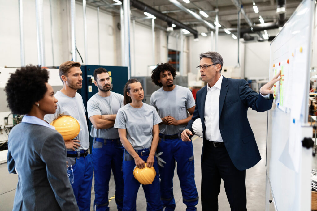 Corporate manager giving a presentation to group of factory workers and talking with them about future business development.