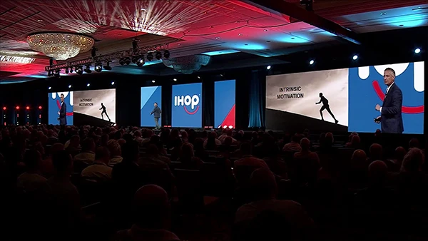 large auditorium with speaker on stage and ihop logo on screen