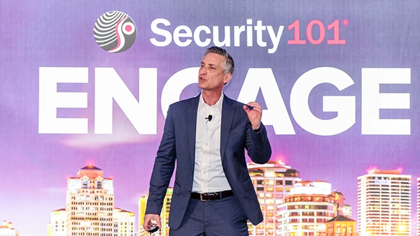 scott greenberg in blue suite standing in front of video screen that says Security 101 Engage