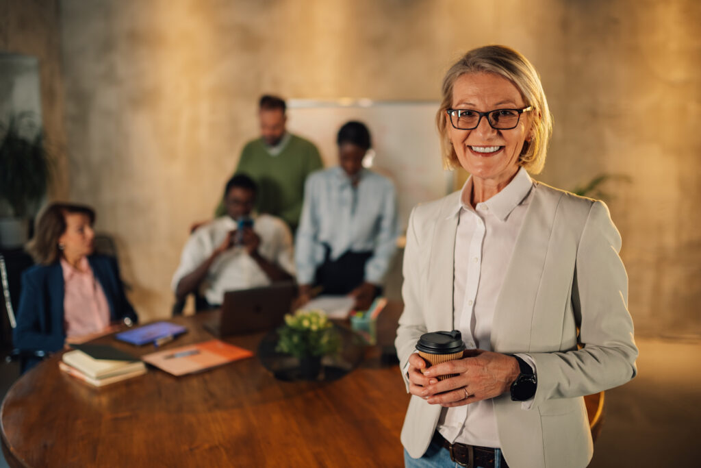 Senior businesswoman with coffee smiling at the camera at office on meeting
