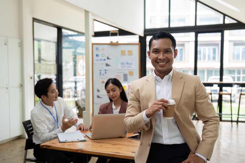 Smiling confident businessman looking at camera and standing in an office at team meeting. Portrait of confident businessman with colleagues in boardroom